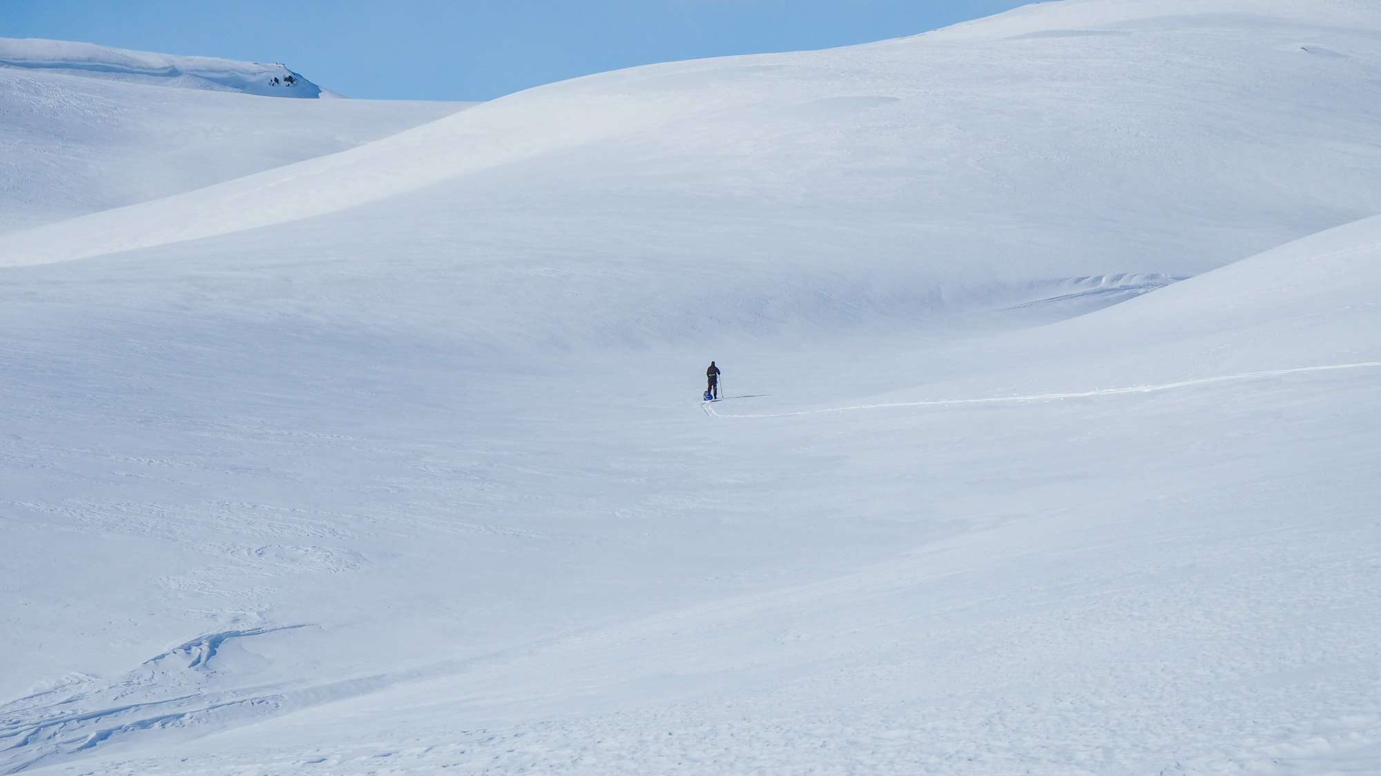 Yksinäinen pieni hahmo hiihtää lumierämaassa. 