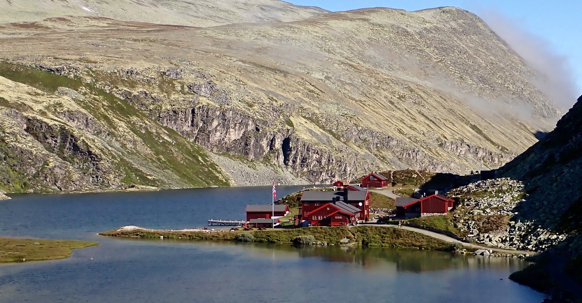 Kuvass kapea tunturijärvi, jonka rannalla punainen talorykelmä. Salossa liehuu Norjan lippu. 