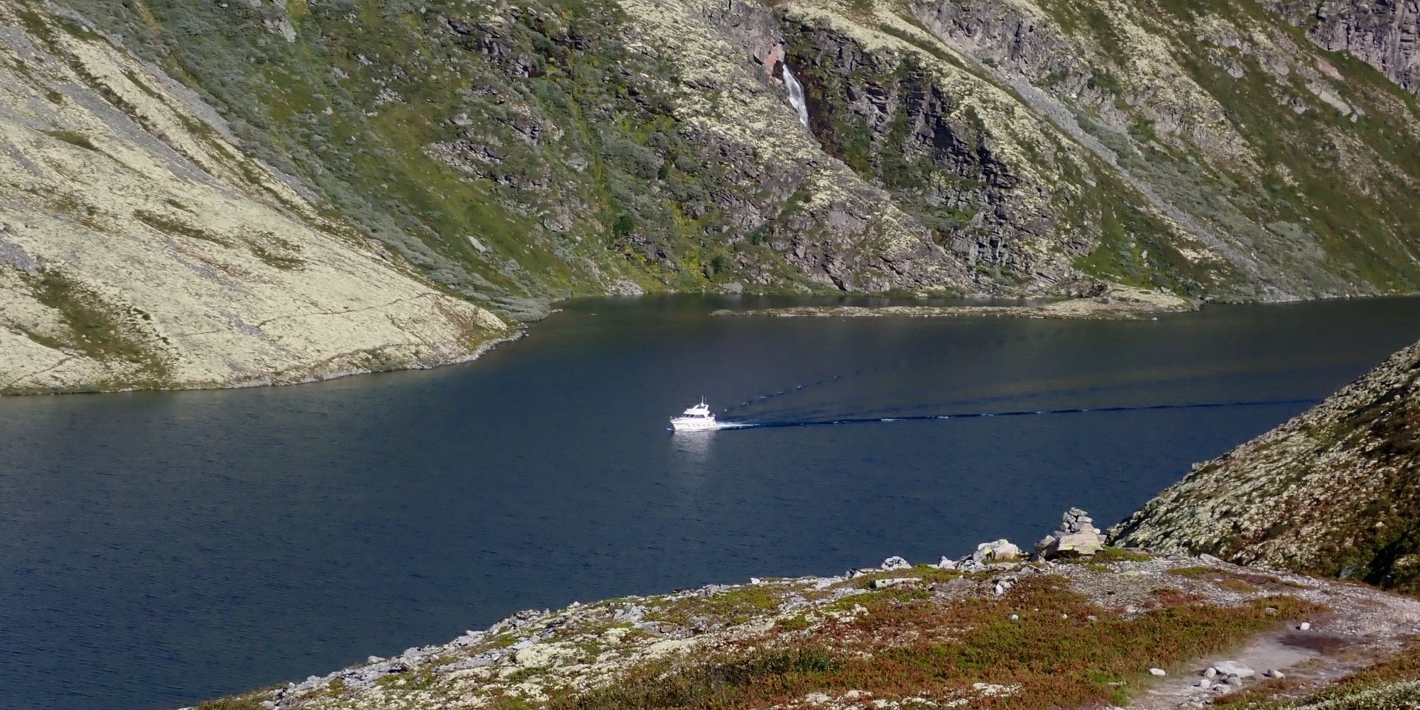 Kuvassa kapea tunturijärvi, jonka keskellä purjehtii kajuutallinen moottorivene.