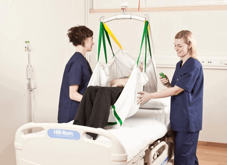 Image of two carers assisting a person in a hoist over a bed