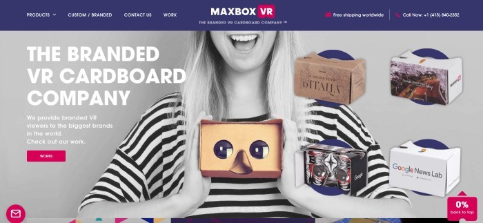 This screenshot of the home page of MaxBox VR has a dark blue navigation bar with white text above a black and white photo of a smiling blond woman holding a cardboard VR viewer, along with white text describing the cardboard viewers made by MaxBox VR.