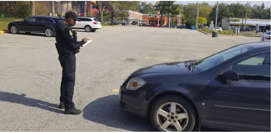 A security Guard in a parking lot givinga  ticket to a car