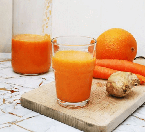 A glass of carrot and orange smoothie with the ingredients alongside