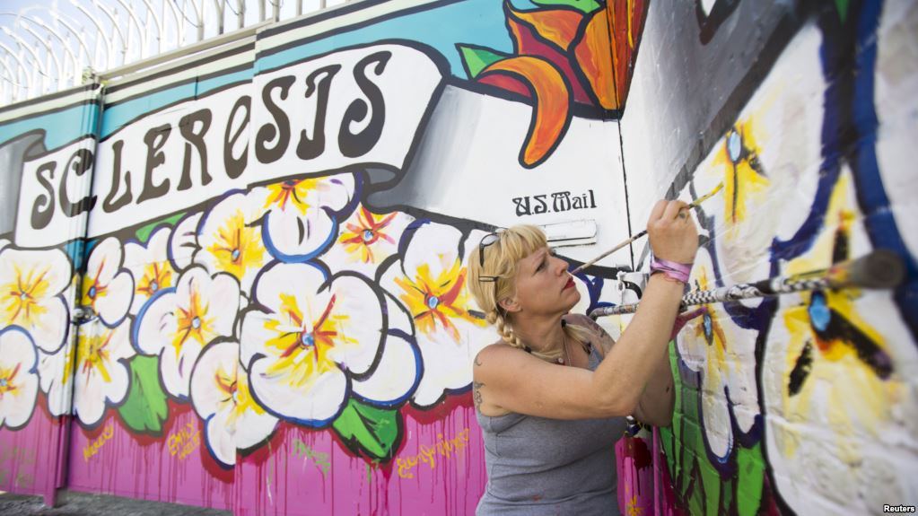 FILE - Street artist Lydia Emily Archibald, who was diagnosed with multiple sclerosis in 2012, touches up her mural aimed at raising awareness about the disease in Los Angeles, April 9, 2015.