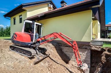 Kellersanierung: Außen- und Innenabdichtung Bagger entfernt Erdreich an Kellerwand eines Einfamilienhauses