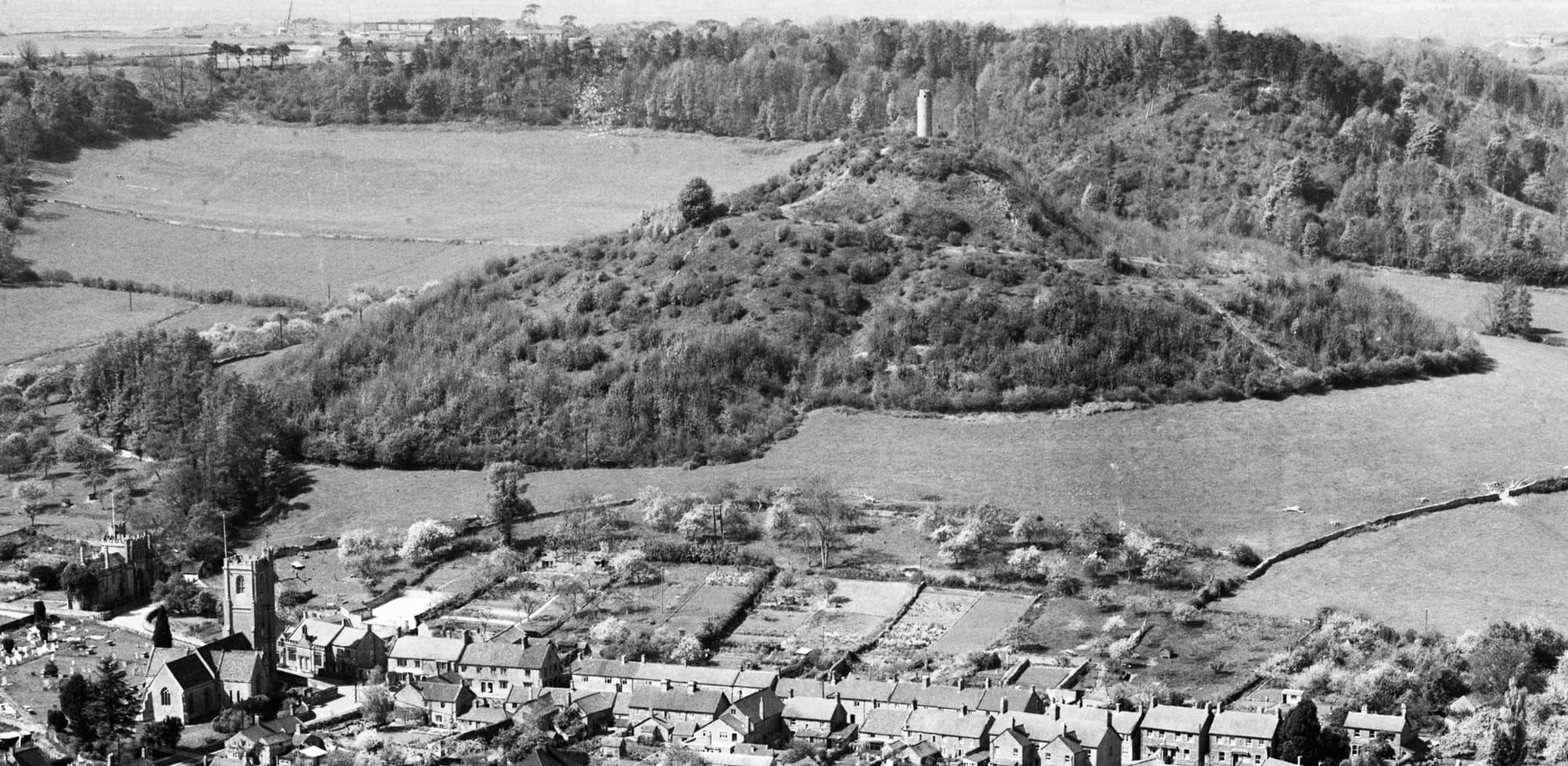 black & white aerial photo taken from above Montacute House showingSt Catherine's church and Bishopstone in the foreground, St Michael's Hill in the middle distance and Hedgecock Hill in the background. St Michael's hill has scrub growth and, because of the lack of mature trees, the extent of the south-east slope of the hill is more apparent than it is today