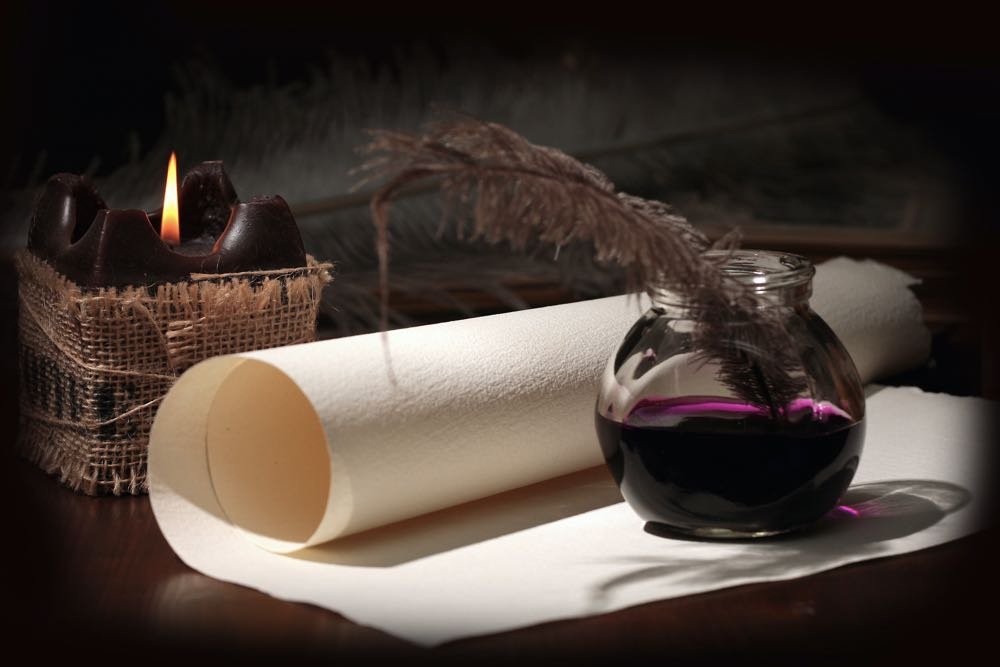 Still life of a scroll of old fashioned paper, a glass ink well of dark purple with a quill by candle light as header image for the About Helena Lind page