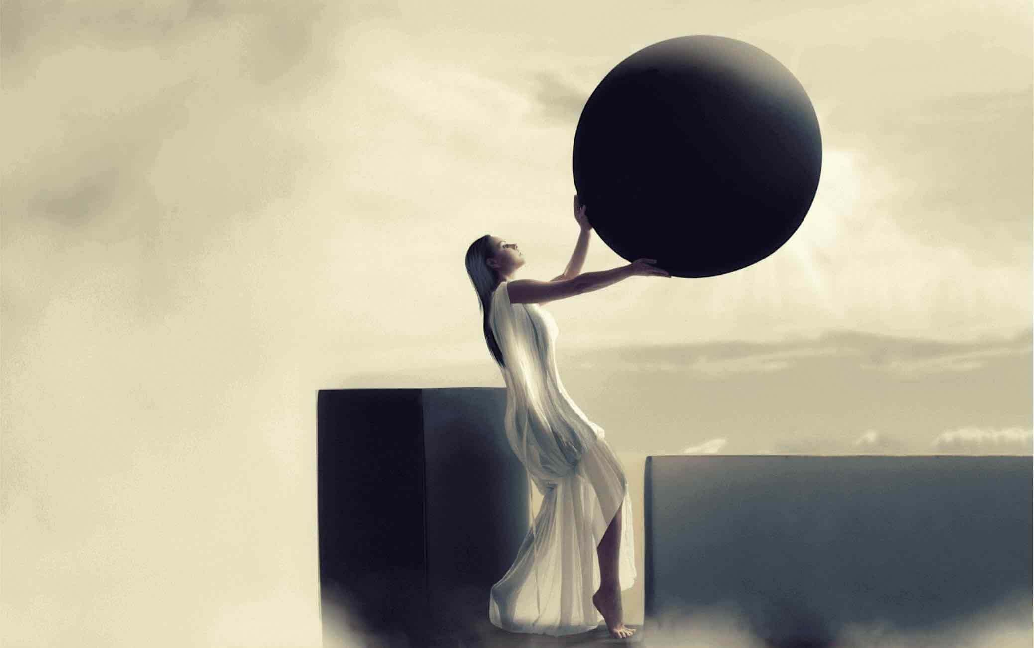 A fine art setting in evening skies showing a serene black haired woman in ancient white dress standing on a black monolith holding a dark sphere or disk as header image for a teaser article about The Destiny Book by Helena Lind