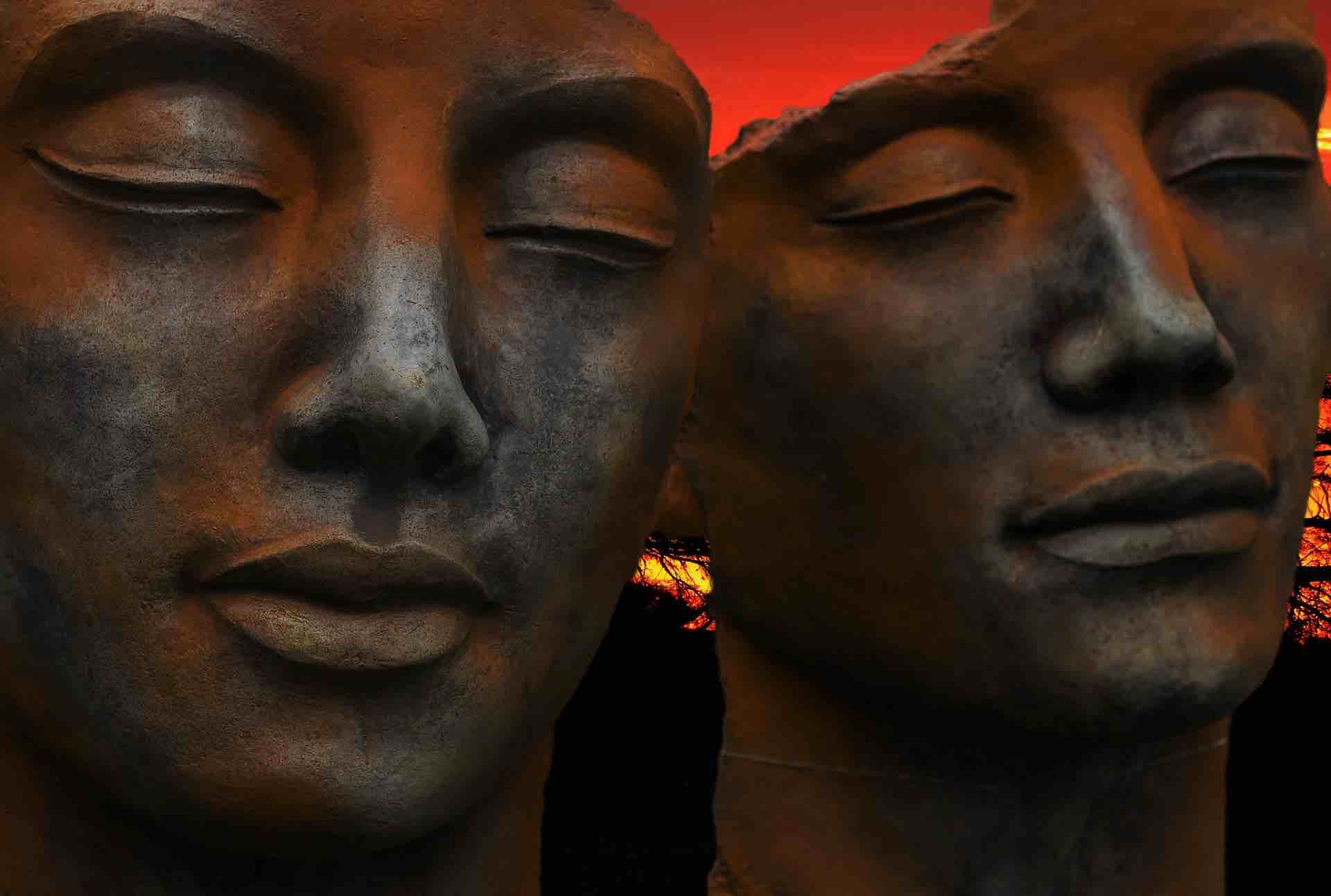 Two serene faces made from burnished metal on a glowing orange-red background as header image for the article Love and Destiny