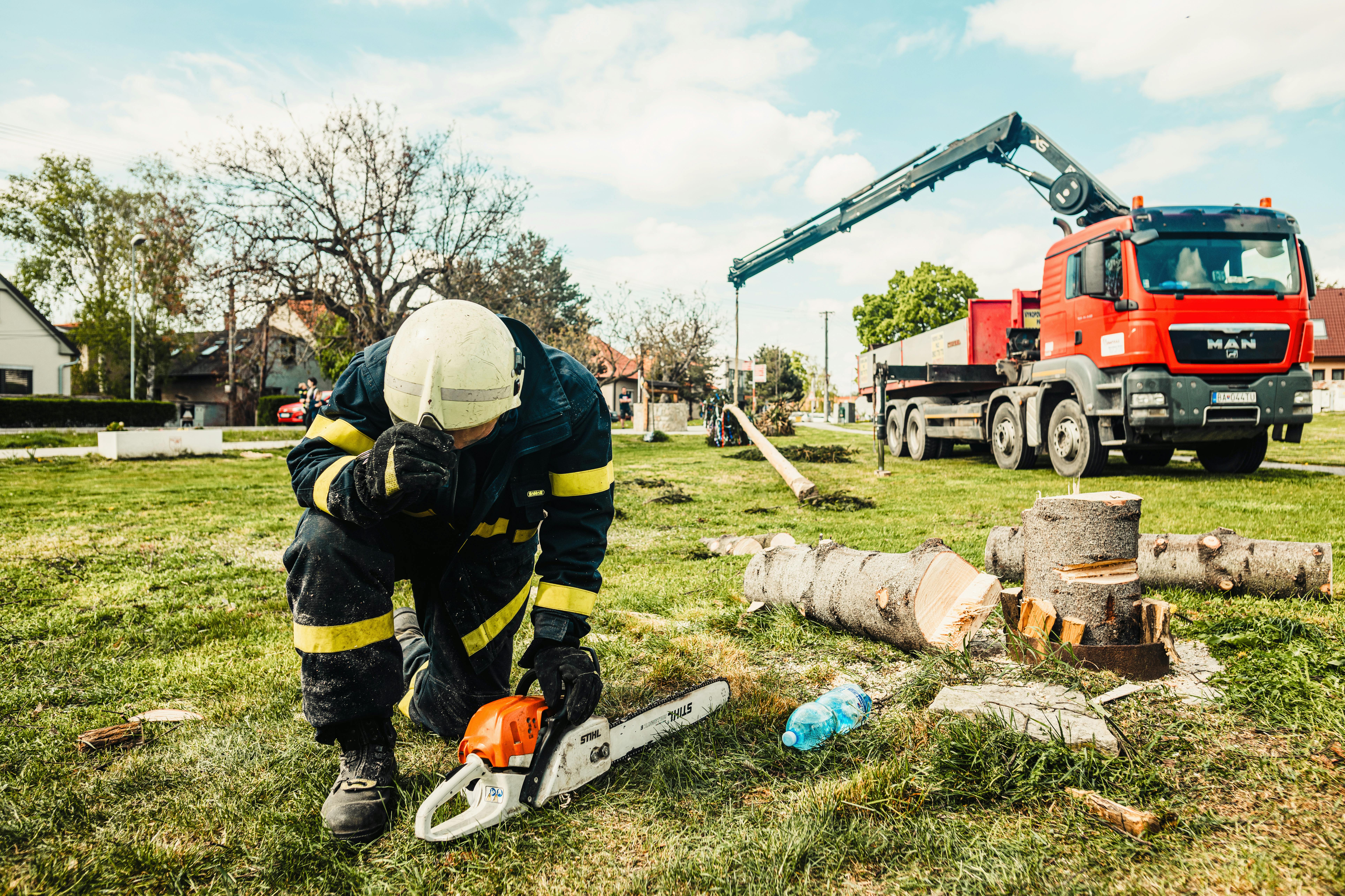 An arborist sitting on the ground with his chainsaw. He's sitting next to a tree that was freshly cut down.