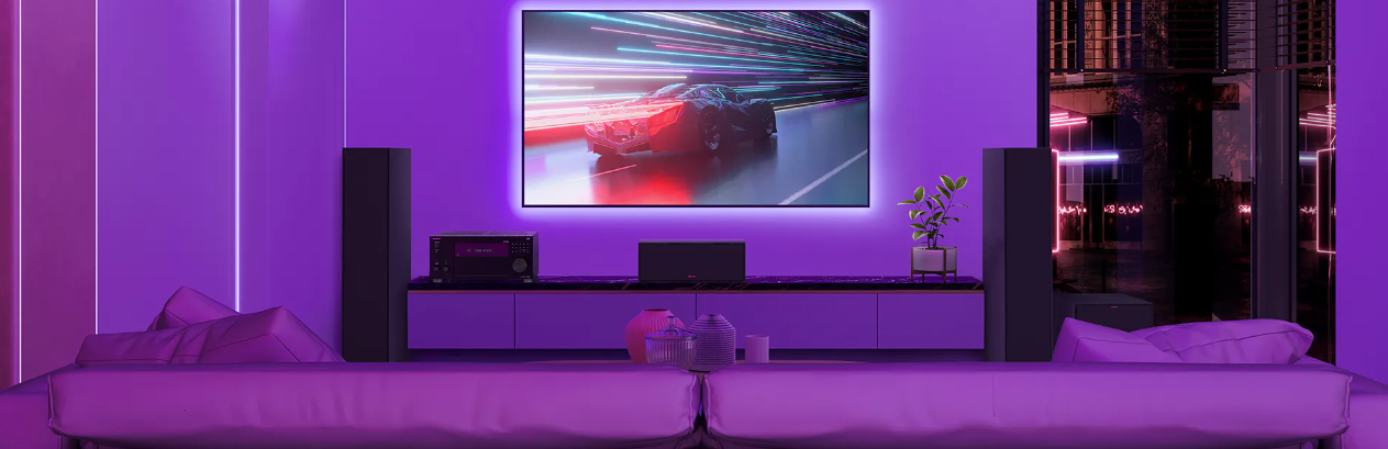 תמונת אוירה של סלון עם תאורה סגולה, רמקולים ריצפתיים ורסיבר אונקיו מונח על שידה מתחת לטלויזיה דולקת 