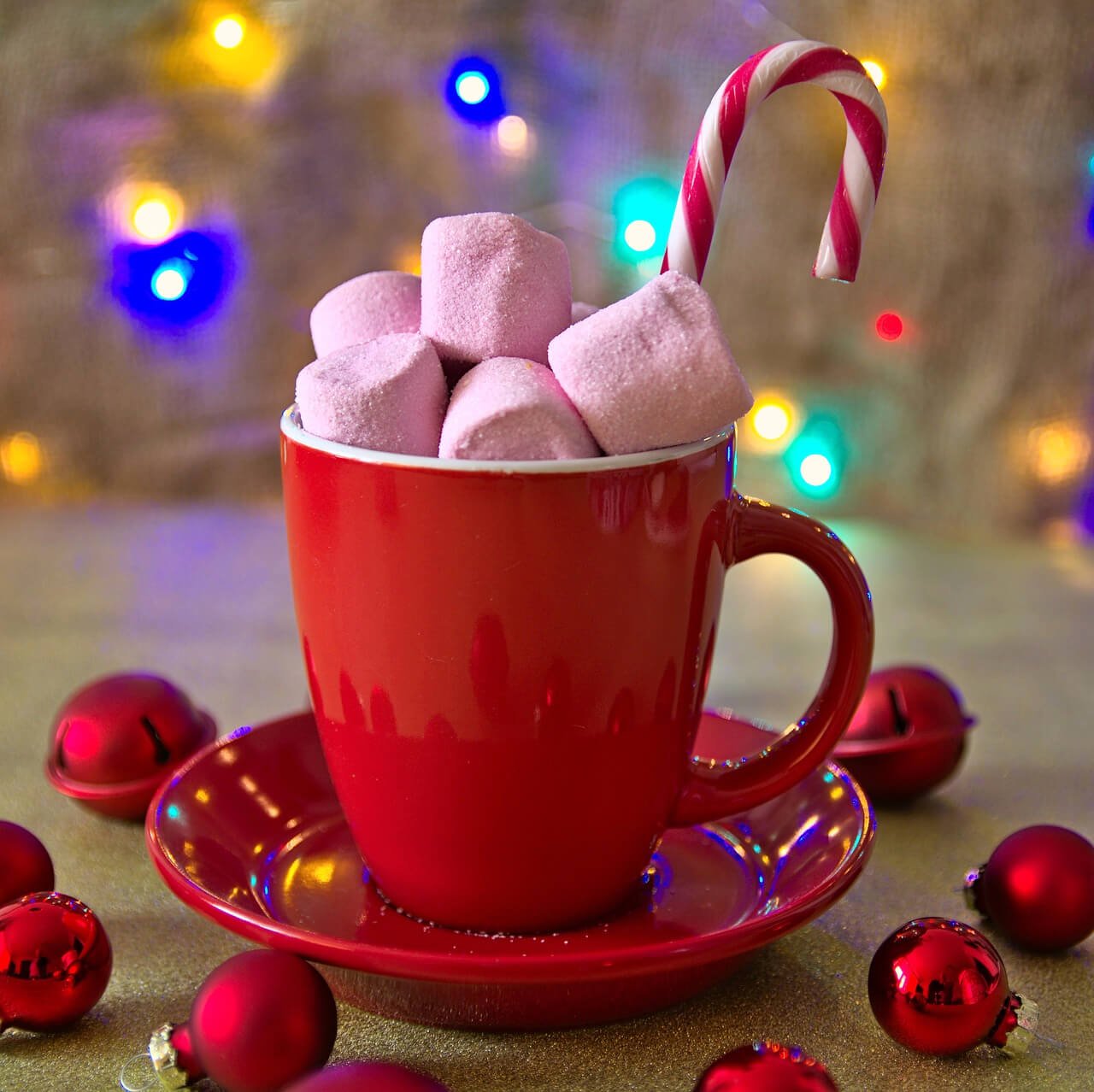 A mini candy can ein a red cup topped with marshmallows, surrounded by Christmas baubles and lights