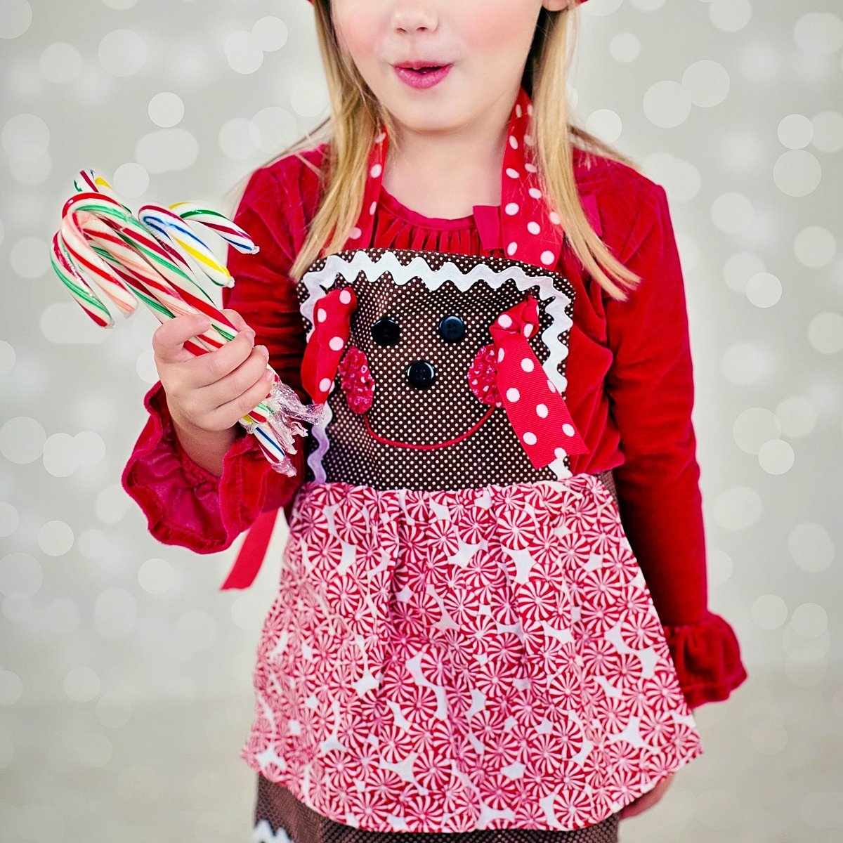 Young girl dressed in Christmas attire holding a bunch of striped candy canes