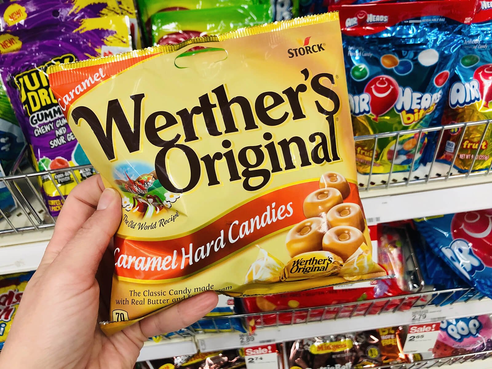 Close-up of a person's hand holding a bag of Werther's Original in a supermarket food aisle.