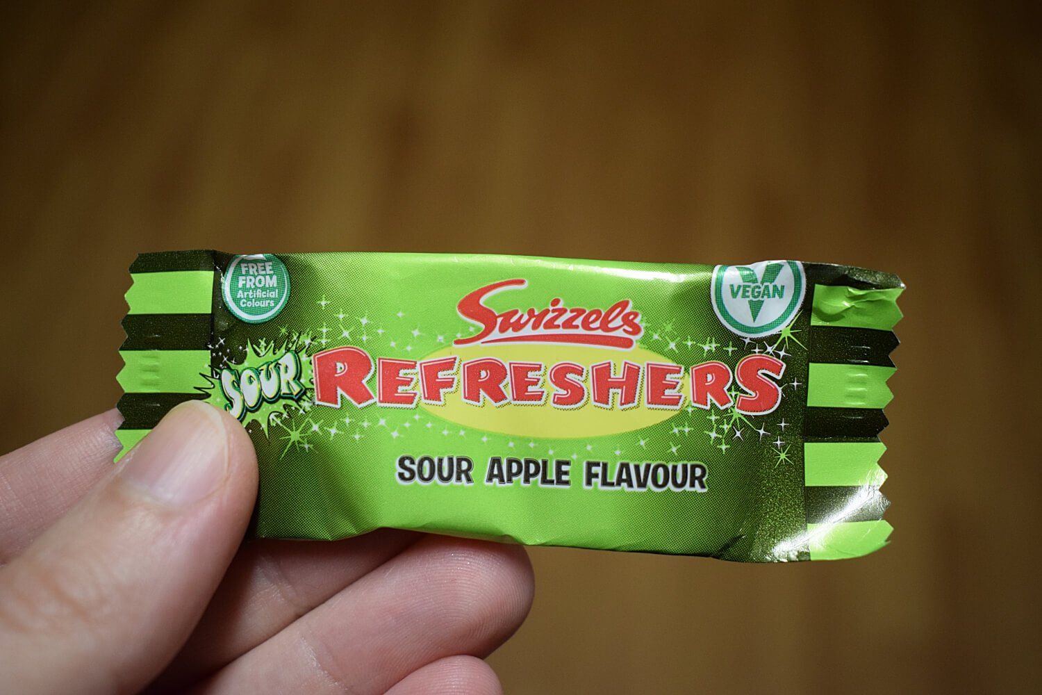Close-up of someone's hand holding Swizzels Refreshers Sour Apple Flavour in green wrapper